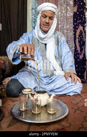 Touareg faisant du thé assis sur le sol sur un tapis. Banque D'Images