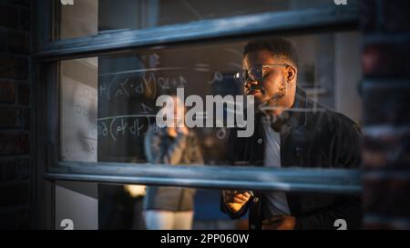 Jeune homme noir expliquant une équation mathématique sur une fenêtre à la maison à un ami féminin en utilisant des marqueurs de verre effaçable. Deux étudiants multiethniques Banque D'Images