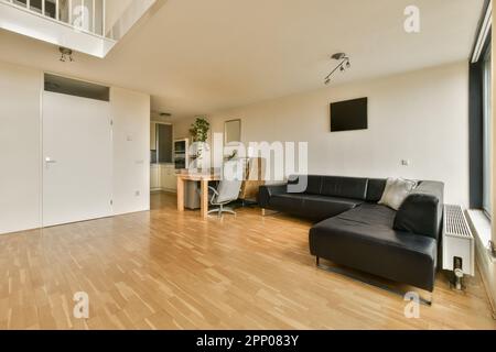 un salon avec parquet et murs blancs au centre de la chambre est un canapé en cuir noir Banque D'Images