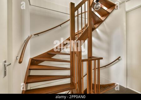 un escalier en colimaçon en bois dans une pièce blanche avec parquet et mains courantes en bois sur le mur derrière Banque D'Images