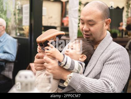Flexible homme bébé tenant ses jambes assis sur les jambes de son père, fils jouant avec son père dans le jardin de bière au pub en Écosse. Joyeux souvenirs. Banque D'Images