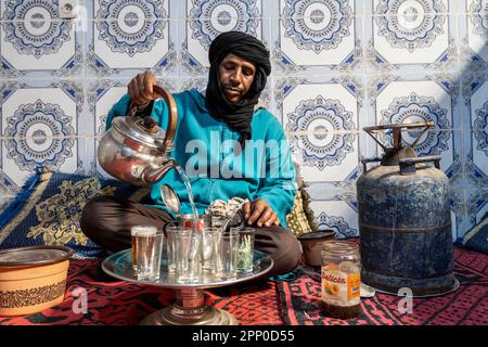 Berbère vêtu de djellaba et de turban noir servant du thé de façon traditionnelle. Banque D'Images