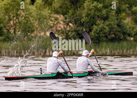 vue latérale des kayakistes mâles sur kayak double dans la course de compétition de kayak, éclaboussures d'eau des pagaies Banque D'Images