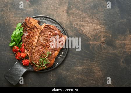 Steaks de l'os en T. Tranché de bœuf grillé en T-bone ou steak de viande de portreuse avec épices romarin et poivre sur un panneau de marbre noir sur fond de bois ancien. À Banque D'Images