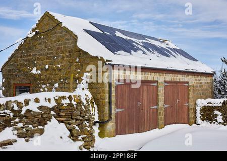 La neige couvre en partie les panneaux solaires sur un double garage le matin après une lourde nuit de neige sur les landes petites exploitations à 900ft dans le North Yorkshire Banque D'Images