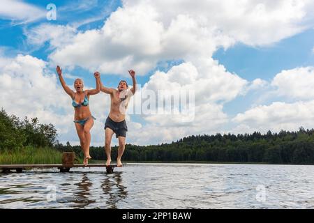 Un couple homme et femme sautant dans l'eau du lac. Vacances d'été dans la nature Banque D'Images
