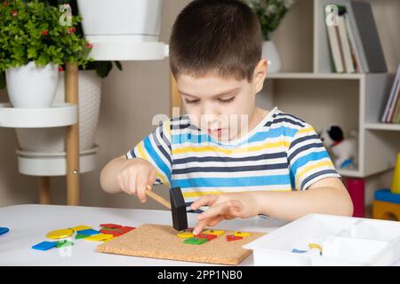 Un enfant d'âge préscolaire joue avec une mosaïque, construit des figures sur une planche, martelant des ongles avec un marteau sur des parties multicolores du concepteur Banque D'Images