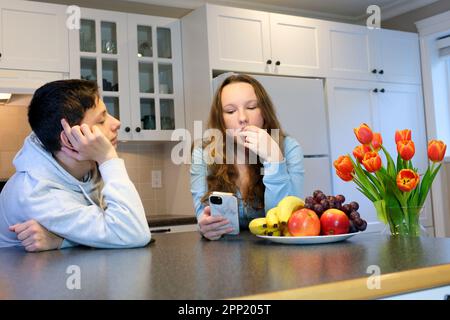 garçon regarde la fille avec amour elle est occupée au téléphone à manger des raisins et à regarder vers le bas des réseaux sociaux gars en amour à regarder un espoir de regard pour une relation demander une date Banque D'Images