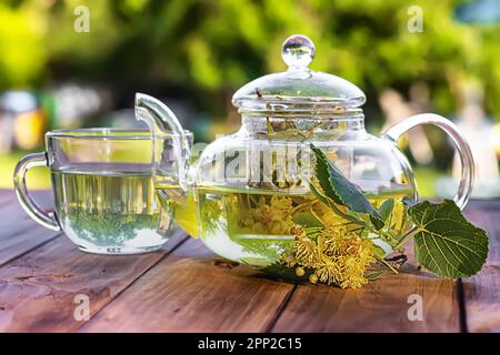 théière en verre remplie de thé au linden et de tranches de lime, assise sur une table en bois dans le jardin Banque D'Images