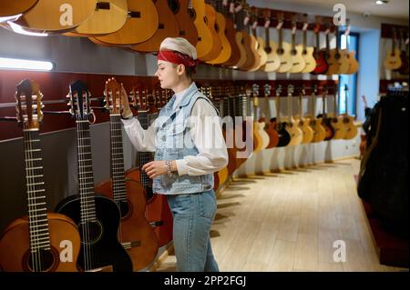 Jeune femme hipster acheteur choisir la guitare acoustique dans la boutique d'instruments Banque D'Images