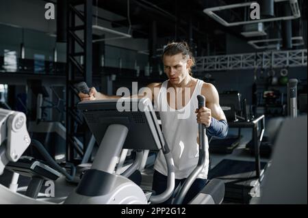 Un sportif en sueur qui fait de l'exercice cardio sur un appareil d'entraînement orbitrack Banque D'Images