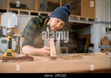 Jeune homme charpentier soufflant de la sciure de bois de planche Banque D'Images