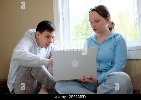 expliquez la leçon garçon montrant la fille sur l'ordinateur aider à étudier des amis frère plus âgé soeur plus jeune en ligne apprenant le temps ensemble assis par fenêtre avec Banque D'Images