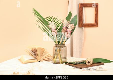 Vase avec ananas décoratif, feuilles de palmier, livre et corde sur la table près du mur beige Banque D'Images