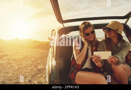 Moments de RoadTrip. deux amis prenant un selfie tout en étant assis dans le coffre d'une voiture. Banque D'Images