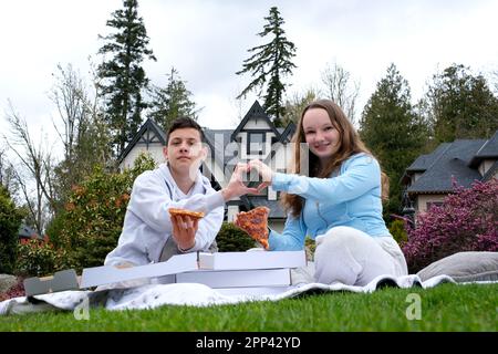 Premier amour première date garçon et fille adolescents manger pizza dans la nature pique-nique faire les mains coeur ensemble confession tendeuse sentiments beaux enfants homme et jeune femme passent du temps ensemble Banque D'Images