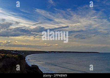 Hunmanby Bay lors d'une soirée de printemps sous un grand ciel bleu et des nuages blancs mis en évidence par le soleil couchant avec la mer éclaboussant contre le fond de la falaise Banque D'Images