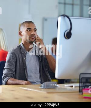 Je suis sûr que nous pouvons faire ce travail. un concepteur parlant sur un téléphone portable tout en travaillant sur un ordinateur dans un bureau. Banque D'Images