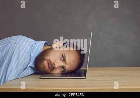 Homme d'affaires indépendant allongé sur un clavier d'ordinateur portable avec une grimace fatiguée sur le visage Banque D'Images