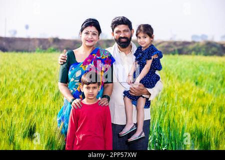 Portrait d'une famille de jeunes agriculteurs indiens heureux debout dans le champ de l'agriculture de blé, parents avec enfants en plein air, concept de l'inde rurale. Banque D'Images