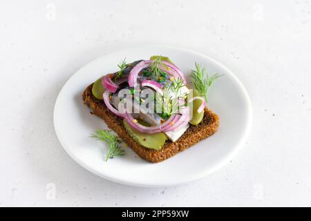 Sandwich avec du poisson de hareng et des cornichons concombres sur une assiette blanche Banque D'Images