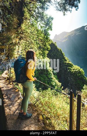 Description: Femme touristique bénéficiant d'une vue depuis le dessous d'un grand mur de roche le long du canal d'eau à la falaise abrupte à travers la forêt tropicale de Madère. Levada de Caldeir Banque D'Images