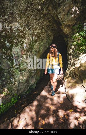 Description: Femme de tourisme sortant d'un tunnel le long d'un sentier de jungle surcultivé à côté d'un canal dans la forêt tropicale de Madère. Levada de Caldeirão Verde, Madère Banque D'Images