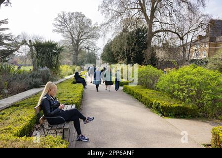 Femme assise sur un banc dans un parc au soleil de printemps ; Walpole Park, Ealing, Londres, Royaume-Uni Banque D'Images