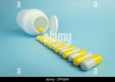 Une pile de pilules jaunes éparpillées d'un pot en plastique blanc sur une table bleue. le concept de médecine de santé et de pharmacie. Production de médicaments. Banque D'Images