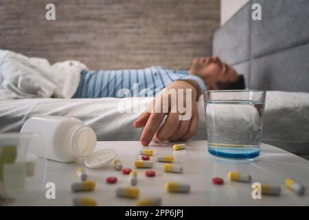 l'homme dort sur un lit. table avec des pilules et un verre d'eau. Somnifères pour un bon sommeil. Homme dormant - pilules sur la table de lit. surdose de médicament. a leth Banque D'Images