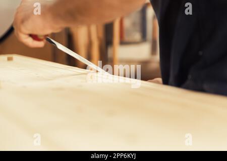 Un artisan se tient avec son couteau à la main. Ce charpentier aime utiliser son outil de coupe manuel parce qu'il désire le contrôle et la capacité de compter s Banque D'Images