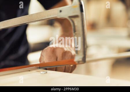 Avec une précision extrême, le menuisier arrête la scie à main avec sa vignette et son index pour travailler sur des inserts en aluminium qui aideront les tiroirs à glisser Banque D'Images