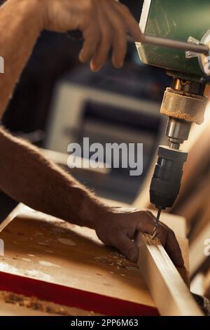 Carpenter utilise une perceuse à colonne dans son atelier. Avec sa main gauche, prenant des risques calculés, il tient et guide le bois, tout en abaissant le levier avec h Banque D'Images