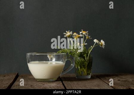 verre de lait et de pâquerettes sauvages sur une table le matin Banque D'Images