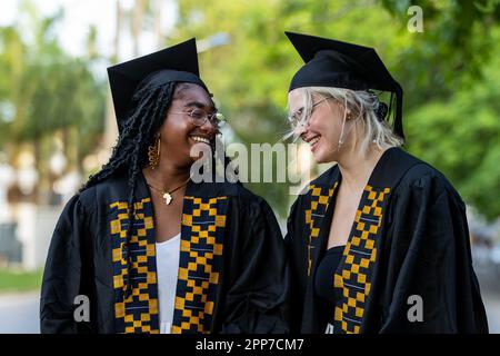 Les jeunes diplômés de l'université d'Afrique noire et du Caucase portant des casquettes et des robes se moquent sur le campus, fiers de la réussite universitaire, des diplômes et de l'obtention de k Banque D'Images