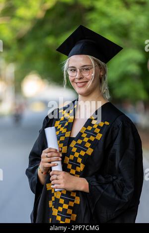 Femme de race blanche, diplômée de l'Université, portant une robe noire et une casquette, titulaire de son certificat de degré, fière de la réussite académique, de succès et de gagner kn Banque D'Images