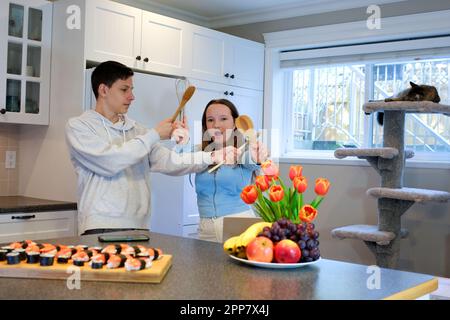 Drôle de famille heureux jeune adolescent appréciant la danse, le chant, sauter dans la cuisine de cuisson ensemble. Gai garçon et fille s'amuser avec l'adolescent fille préparant un repas sain à la maison. Banque D'Images