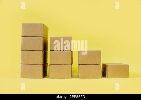 Les boîtes en carton kraft fermées sont empilées dans une rangée descendante sur un fond jaune. Concept de livraison et de stockage des marchandises. Banque D'Images
