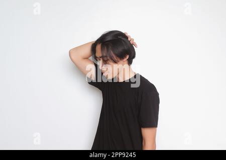 Portrait d'un bel homme asiatique en t-shirt noir à cheveux longs. Modèle posé tout en lissant les cheveux à la main. Image isolée sur fond blanc Banque D'Images