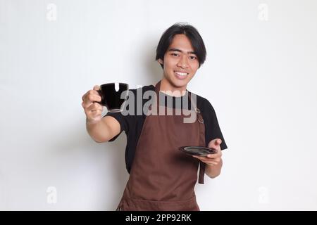 Portrait d'un joli barista asiatique en tablier marron servant une tasse de café au client. Image isolée sur fond blanc Banque D'Images