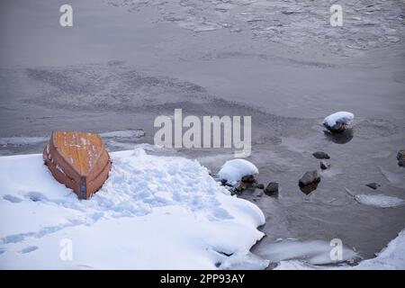 Paysage d'hiver de l'Altaï avec la rivière Biya. L'eau coule entre les berges enneigées. Un bateau renversé se trouve sur la glace près de la rive. Banque D'Images