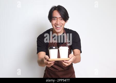 Portrait d'un joli barista asiatique en tablier marron tenant deux tasses de café en papier à emporter. Image isolée sur fond blanc Banque D'Images