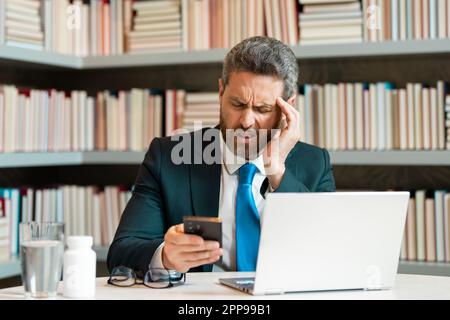 L'homme d'affaires a eu la migraine touche sa tête à cause de la douleur. Homme responsable avec un gros mal de tête travaillant sur un ordinateur portable. Travailleur indépendant ou responsable chez de Banque D'Images