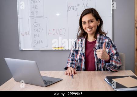 Enseignante et étudiante ayant une conférence en ligne, à l'aide d'un ordinateur portable. Femme tuteur leçon étrangère souriant et montrant le pouce vers le haut satisfaisant avec Banque D'Images