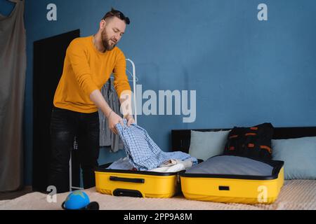 Homme adulte empaquant des vêtements dans une valise sur le lit à la maison, se préparant pour le voyage, concept de voyage de vacances. Banque D'Images