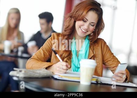 Terminer son travail en déplacement. Une belle jeune étudiante de l'université utilisant son smartphone dans une boutique de café pendant ses études. Banque D'Images