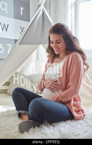 J'en rêvais depuis si longtemps. une femme enceinte se touchant le ventre tout en étant assise à la maison. Banque D'Images