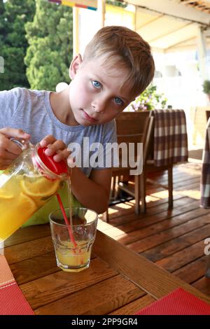 Un enfant verse de la limonade de la verseuse dans un verre au restaurant Banque D'Images