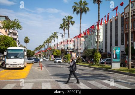 Un homme parlant sur un téléphone portable traverse une route bordée de palmiers et de banderoles avec le drapeau turc à Alanya, dans la province d'Antalya, en Turquie. Banque D'Images