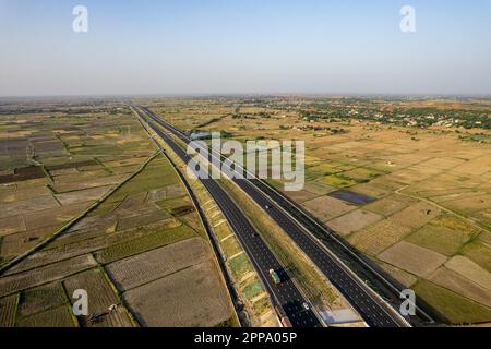 tir de drone aérien à trépied verrouillé de new delhi mumbai jaipur express autoroute surélevée montrant six voies de route avec des feids verts avec des fermes rectangulaires Banque D'Images